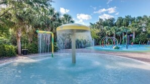 Un espace aquatique agrémenté d’une fontaine centrale, entouré d’une aire de jeux avec des balançoires et des toboggans.