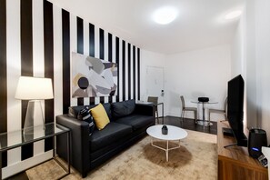 Un salon moderne avec un canapé noir, une table basse, un téléviseur et un tableau accroché au mur.