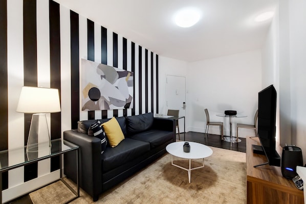 A modern living room with a black sofa, a coffee table, a TV, and a painting on the wall.
