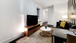 Een moderne woonkamer met een flatscreen televisie, een klein rond tafeltje, een bank met een geel kussen en een 'Niet roken'-bord.