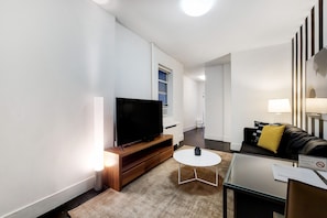 Un salon moderne avec un téléviseur à écran plat, une petite table ronde, un canapé agrémenté d’un coussin jaune et un panneau indiquant « Il est interdit de fumer ».
