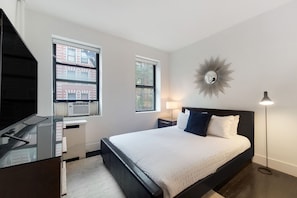 A modern bedroom with a large bed, a desk, and two windows.