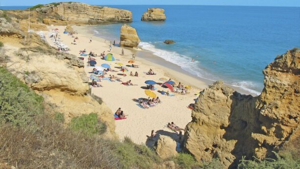 A beach with rocky cliffs, clear blue water, and people sunbathing.