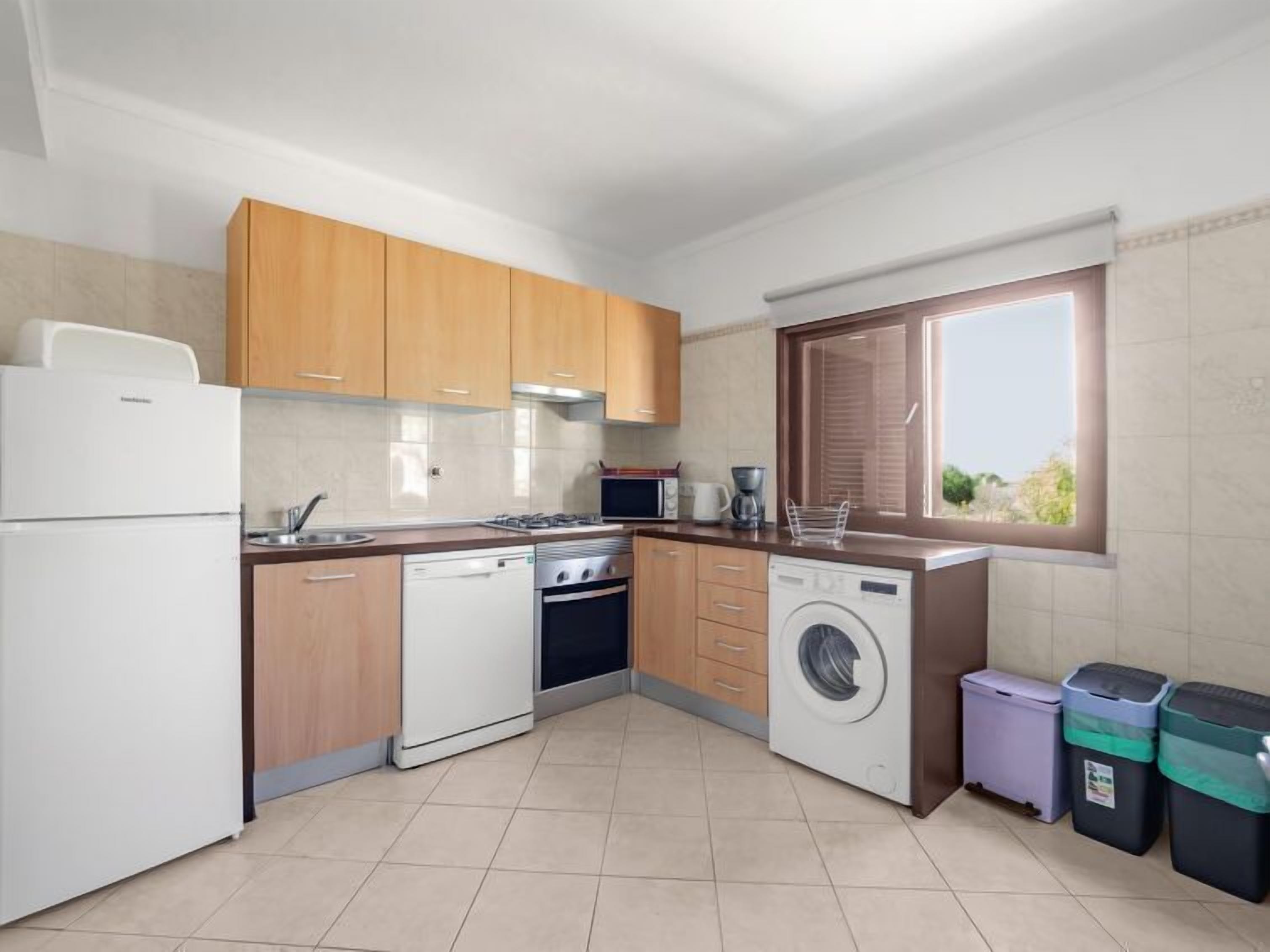 A modern kitchen with wooden cabinets, a dishwasher, a stove, a microwave, and a window with blinds.