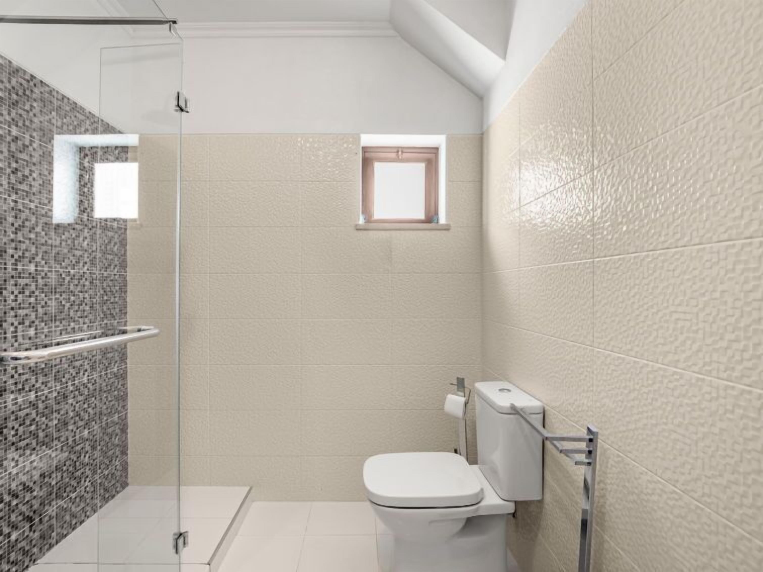 A modern bathroom with a glass shower enclosure, a toilet, and a small window.