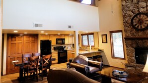 A spacious living area with a dining table and chairs, a fireplace, and a kitchen with wooden cabinets and a stone accent wall.