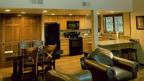 A spacious living room with a leather sofa and dining area, a kitchen with wooden cabinets and modern appliances, and a large window providing natural light.