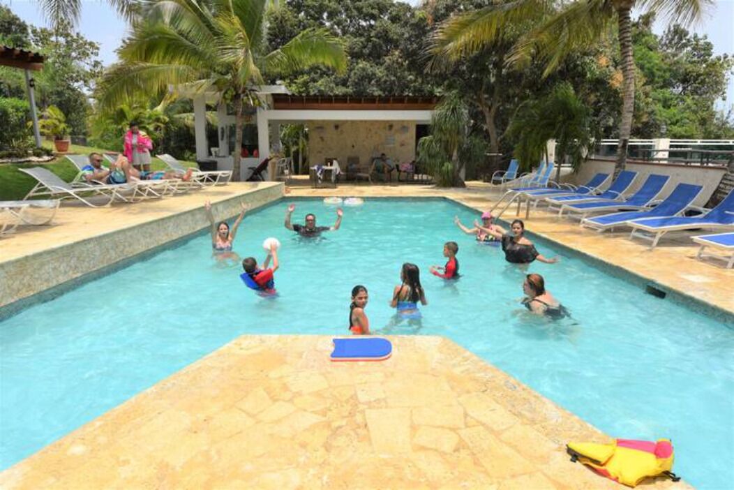 A swimming pool with people enjoying the water, surrounded by lounge chairs and palm trees.