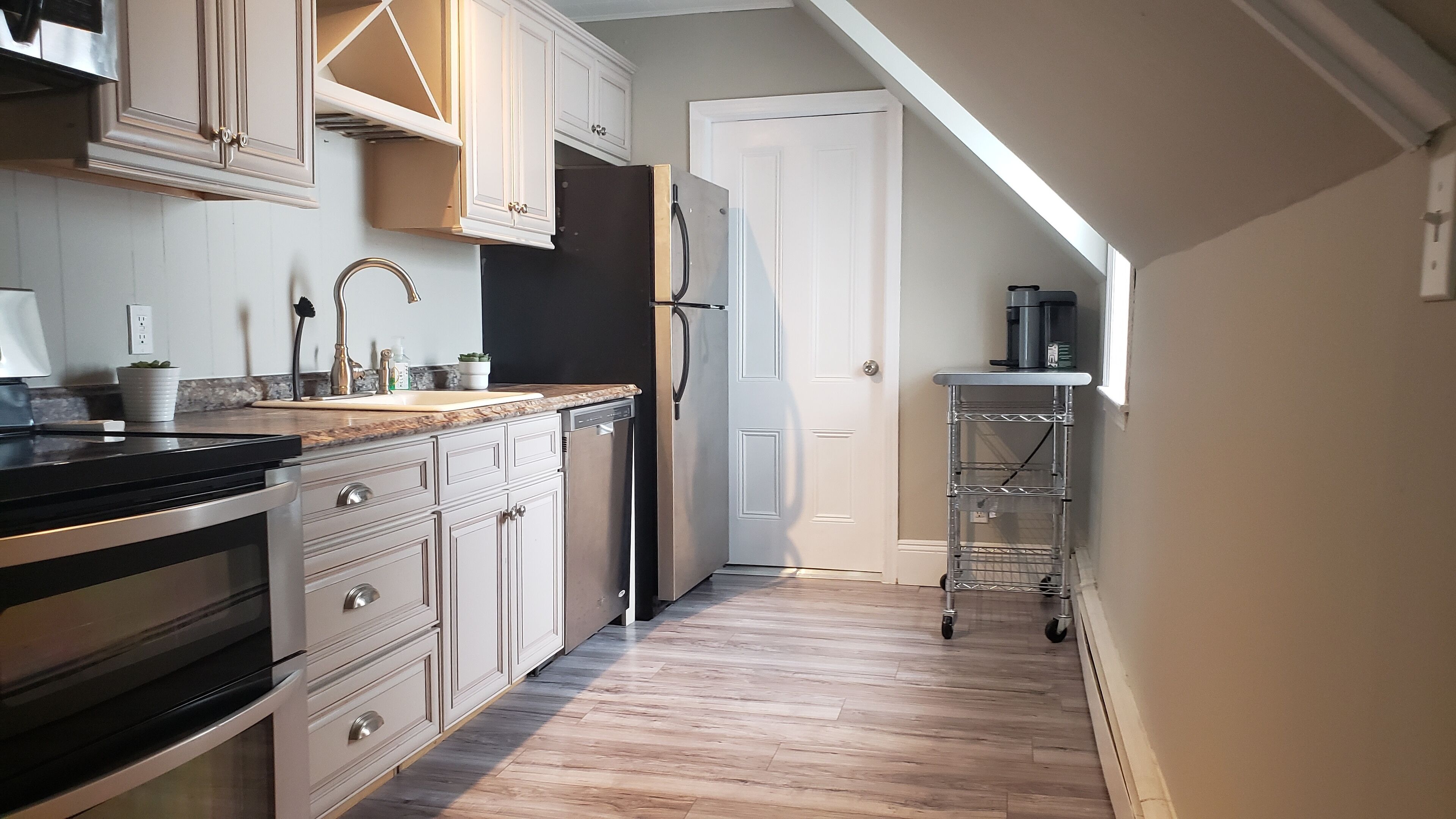 Una cocina moderna con armarios blancos, un refrigerador de acero inoxidable y una encimera con una cafetera.