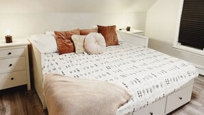 A bedroom with a bed, two bedside tables, a window with blinds, and a nightstand with a candle. - Rosé All Day King Studio | Retro Vibes | Downtown| (Fredericton)