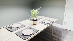 A dining table set with placemats, plates, and cutlery, with a potted plant in the center. - Rosé All Day King Studio | Retro Vibes | Downtown| (Fredericton)