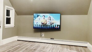 A room with a flat-screen TV mounted on a wall, a window with a white frame, and a wooden floor. - Rosé All Day King Studio | Retro Vibes | Downtown| (Fredericton)