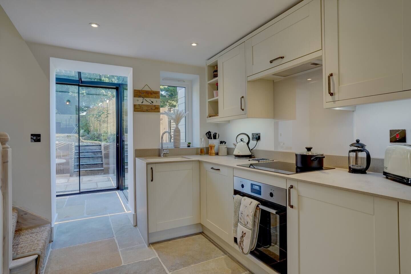 A modern kitchen with a built-in oven, a sink, and a stove. There is a window providing natural light and a view of the outside.
