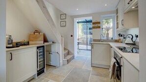Una cocina moderna con armarios blancos, horno integrado y un refrigerador pequeño. Hay una escalera que lleva a un balcón con puerta de vidrio.