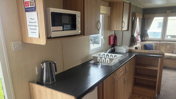 A compact kitchenette with a microwave, kettle, sink, and storage cabinets.