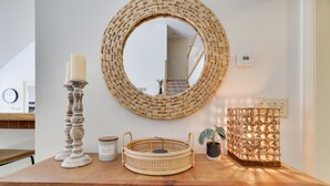 Een houten dressoir met een geweven spiegel, een kaars, een dienblad en een lantaarn.