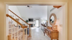 Een ruime woonkamer met een houten trap, een grote spiegel en een eethoek met stoelen.