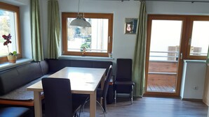 A dining area with a table, chairs, a bench, and a view through a window.