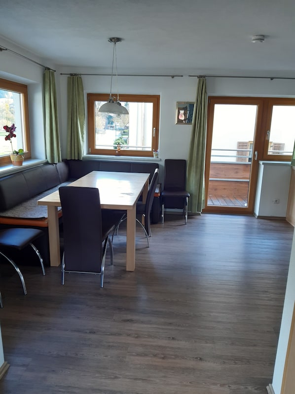 A dining area with a table, chairs, a bench, and a view through a window.