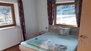 A bedroom with a wooden bed, a nightstand, a window with curtains, and a view of a landscape.