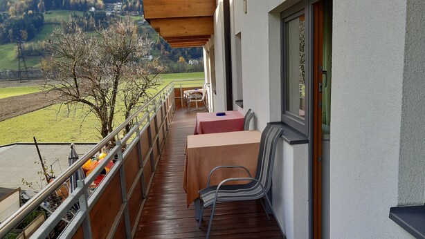 A wooden deck with a table and chairs, overlooking a rural landscape with fields and hills.