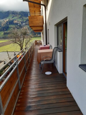 A wooden deck with a table and chairs, overlooking a rural landscape with fields and hills.