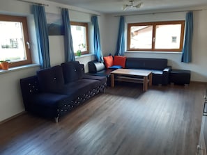 A modern living room with a dark sofa, a wooden coffee table, and a window with blue curtains.