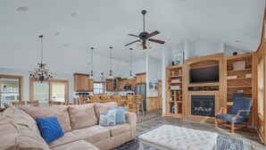 A spacious living room with a beige sectional sofa, a white ottoman, and a wooden entertainment unit with a TV and fireplace. - 5566- Pearl Jam - Nags Head Retreat w/ Pool, Hot Tub & Theater (Nags Head)