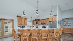 A modern kitchen with wooden cabinets, a central island with bar stools, and pendant lighting. - 5566- Pearl Jam - Nags Head Retreat w/ Pool, Hot Tub & Theater (Nags Head)