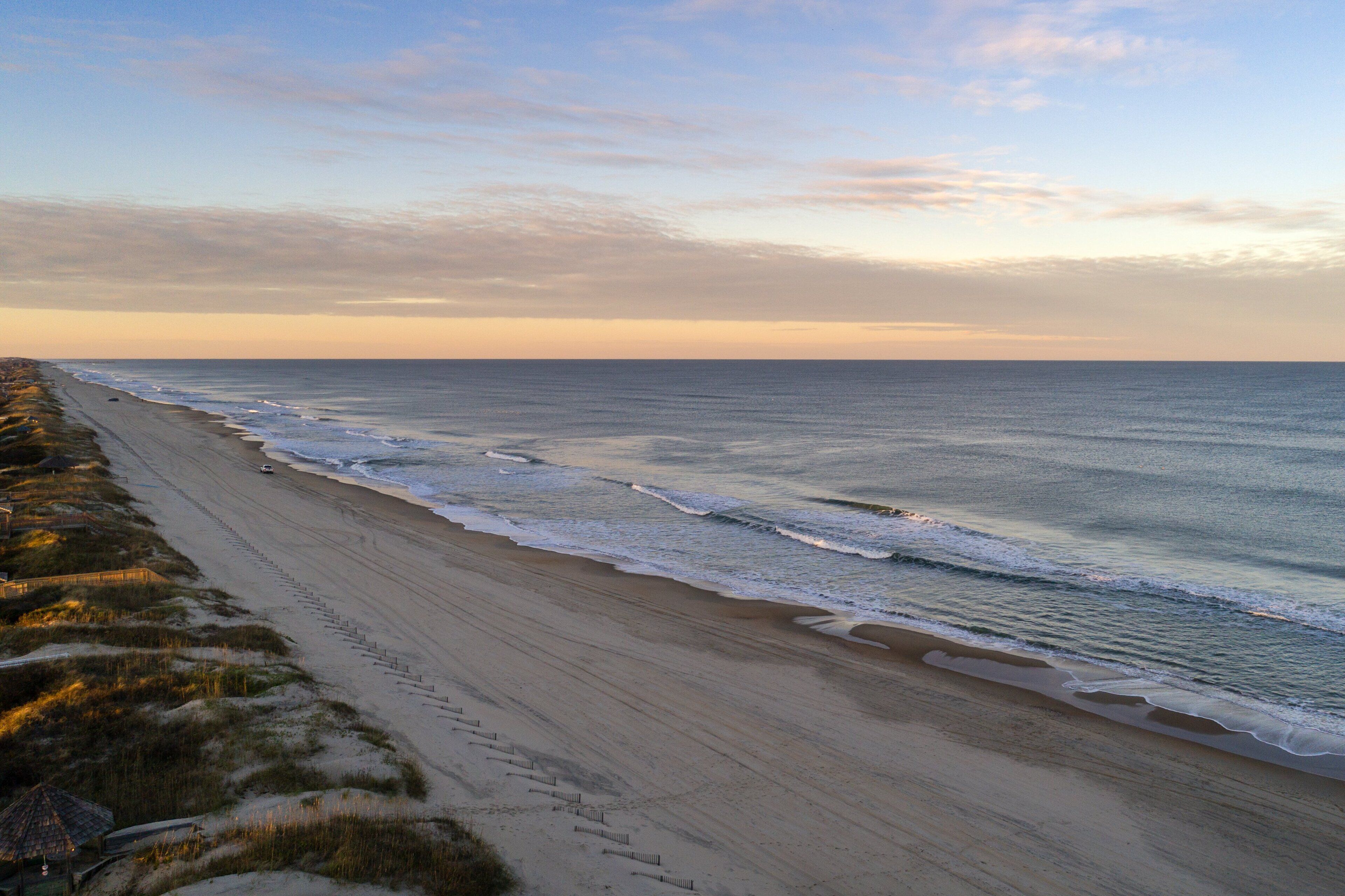 Une plage avec une longue étendue de sable et quelques bâtiments visibles au loin.