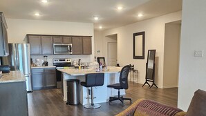 A modern kitchen with a central island, a dining area with a sofa, and a hallway leading to a bedroom.