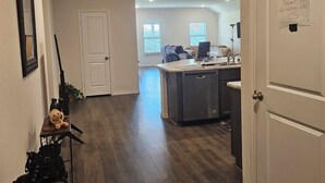 A hallway with a wooden floor, a white door, a small table with a teddy bear, and a rack with shoes.