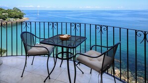 Ein Balkon mit Tisch und Stühlen mit Blick auf das klare, blaue Meer und eine entfernte Insel.