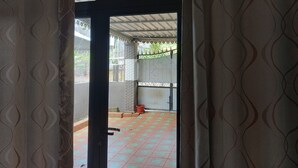 Une porte ouverte donnant sur un patio abrité, doté d’un sol carrelé et d’une clôture en métal.