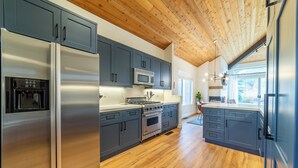 A modern kitchen with grey cabinets, stainless steel appliances, and a wooden ceiling. - Snowcreek Luxury Remodel 529 (Mammoth Lakes)