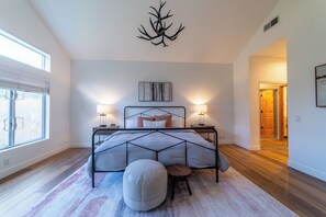 A modern bedroom with a large bed, two bedside tables, a wall-mounted artwork, and a view through a window. - Snowcreek Luxury Remodel 529 (Mammoth Lakes)