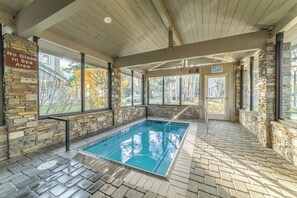 An indoor swimming pool with stone walls and a wooden ceiling, surrounded by large windows. - Snowcreek Luxury Remodel 529 (Mammoth Lakes)