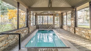 An indoor swimming pool with stone walls and a wooden ceiling, surrounded by large windows. - Snowcreek Luxury Remodel 529 (Mammoth Lakes)
