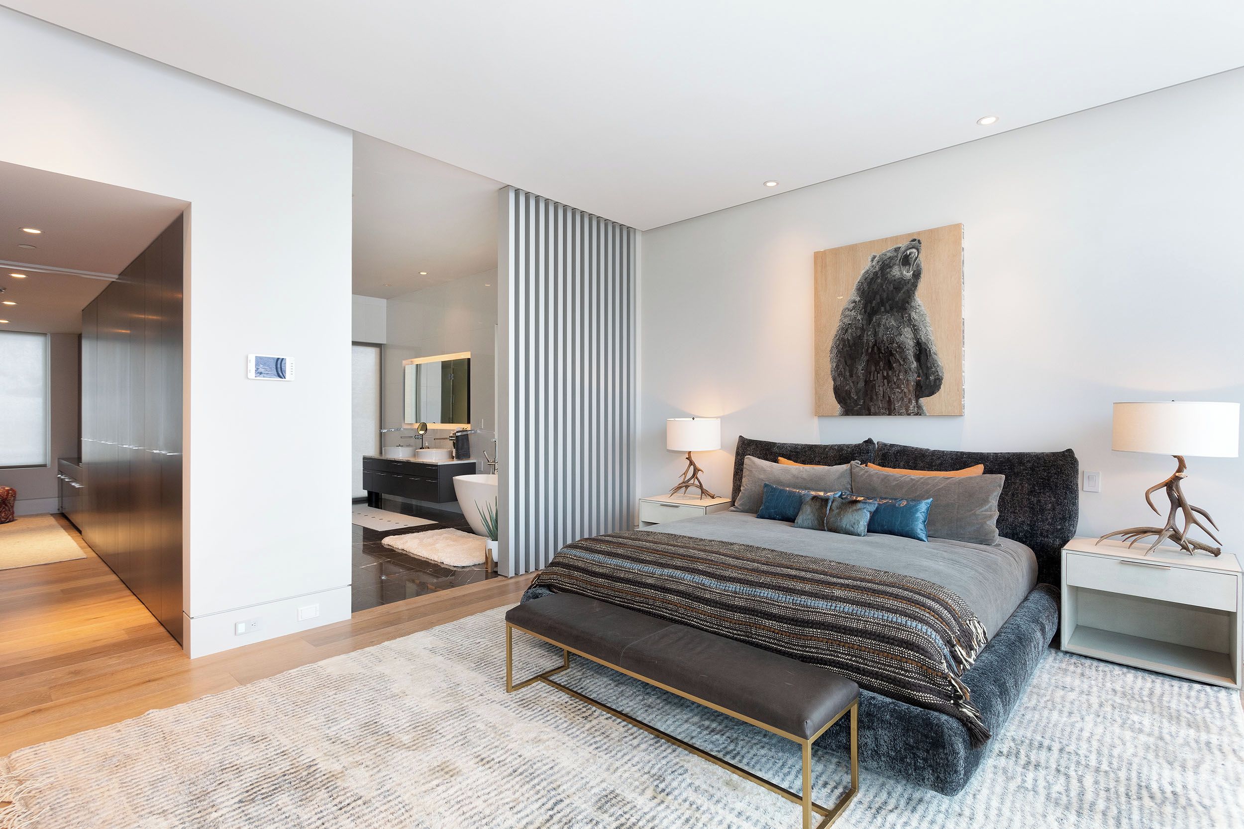 Une chambre à coucher moderne avec un grand lit, des tables de chevet, un banc et une œuvre d’art accrochée au mur.