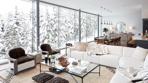 A modern living room with a large window, a white sofa, a glass coffee table, and a fireplace. - Kadenwood 2980 – Ski in Ski out, Private Pool, Hot Tub & Gondola (Whistler)