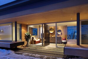 Una casa moderna con entrada de vidrio, un interior acogedor con un sofá y un comedor, y vistas a un paisaje nevado.