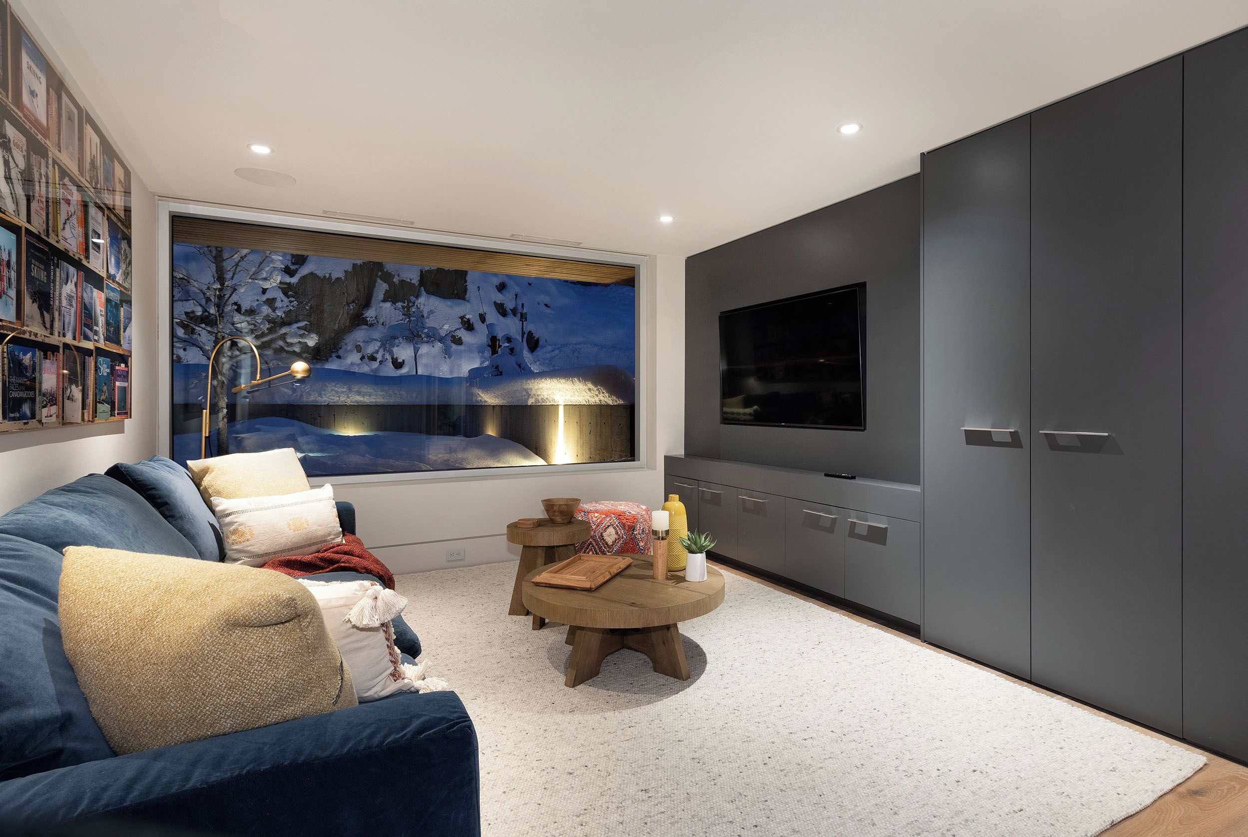 A modern living room with a large window, a flat-screen TV, a bookshelf, and a cozy seating area.