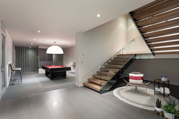 A modern living room with a pool table, a staircase with glass railings, and a cozy seating area. - Kadenwood 2980 - Ski in Ski out, Private Pool, Hot Tub & Gondola (Whistler)