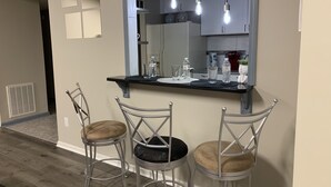 Una cocina moderna con una encimera negra, tres taburetes altos y un espejo grande sobre la encimera.