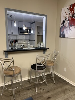 A kitchen with a bar area, two metal chairs, and a modern light fixture.