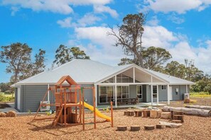 Una casa con un porche amplio, un parque infantil de madera y un espacio exterior cubierto.