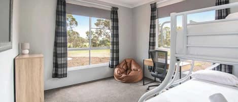 Un dormitorio con cama, escritorio, silla, puf y ventana con cortinas.
