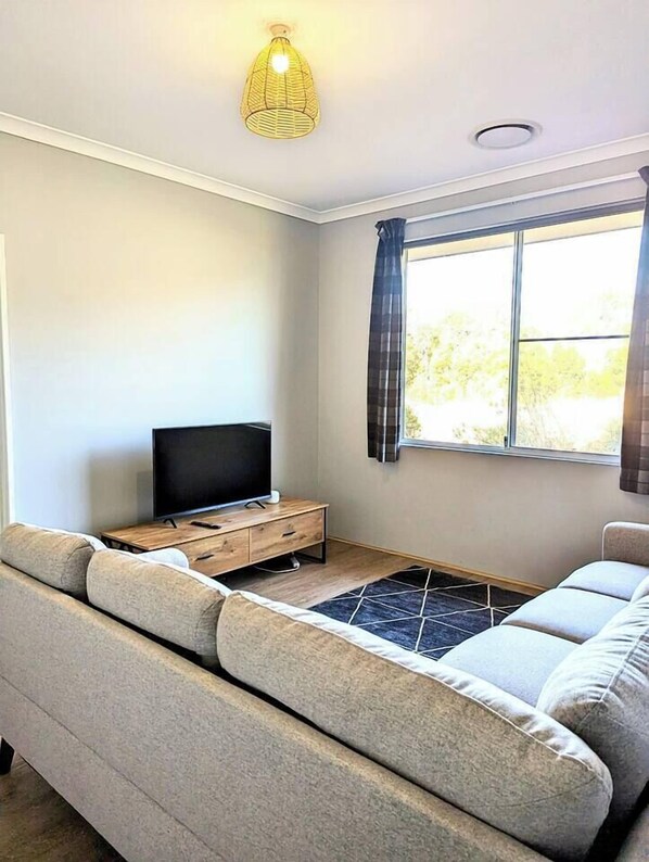 Una sala de estar moderna con un sofá, un televisor sobre un mueble de madera y una ventana con cortinas.