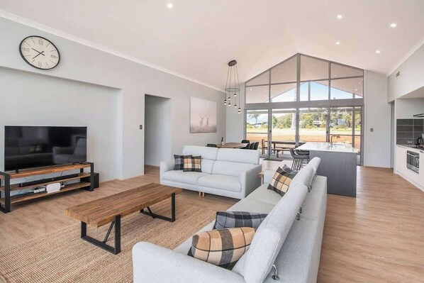 A modern living room with a flat-screen TV, a sofa set, a coffee table, and a large window offering a view.