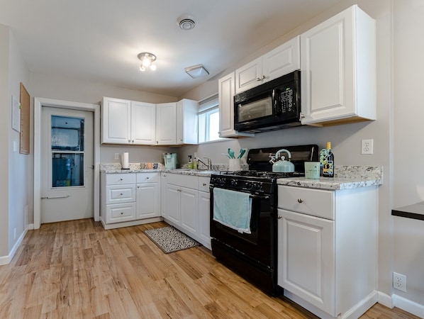 A kitchen with white cabinets, a black stove, a microwave, and a tiled backsplash.